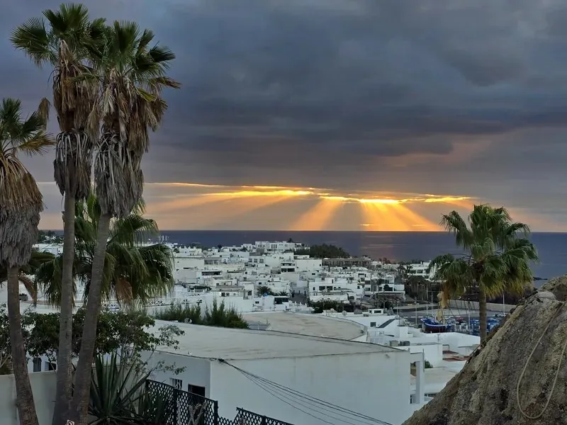 Pueblo de casas blancas y palmeras con rayos de sol sobre el mar