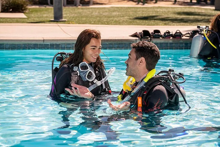 Instructora y alumno conversan dentro de una piscina con el equipo puesto