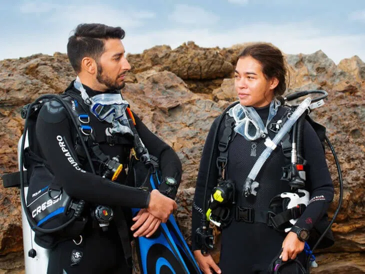 Instructor e instructora con equipo completo conversan antes de la inmersión