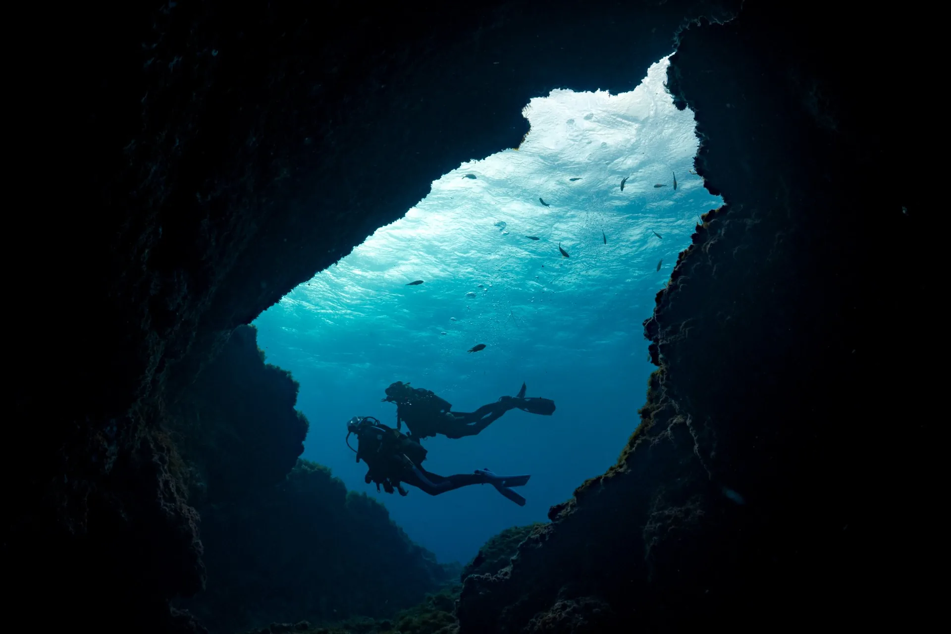 Buceador en silueta dentro de una cueva con una abertura azul hacia la superficie