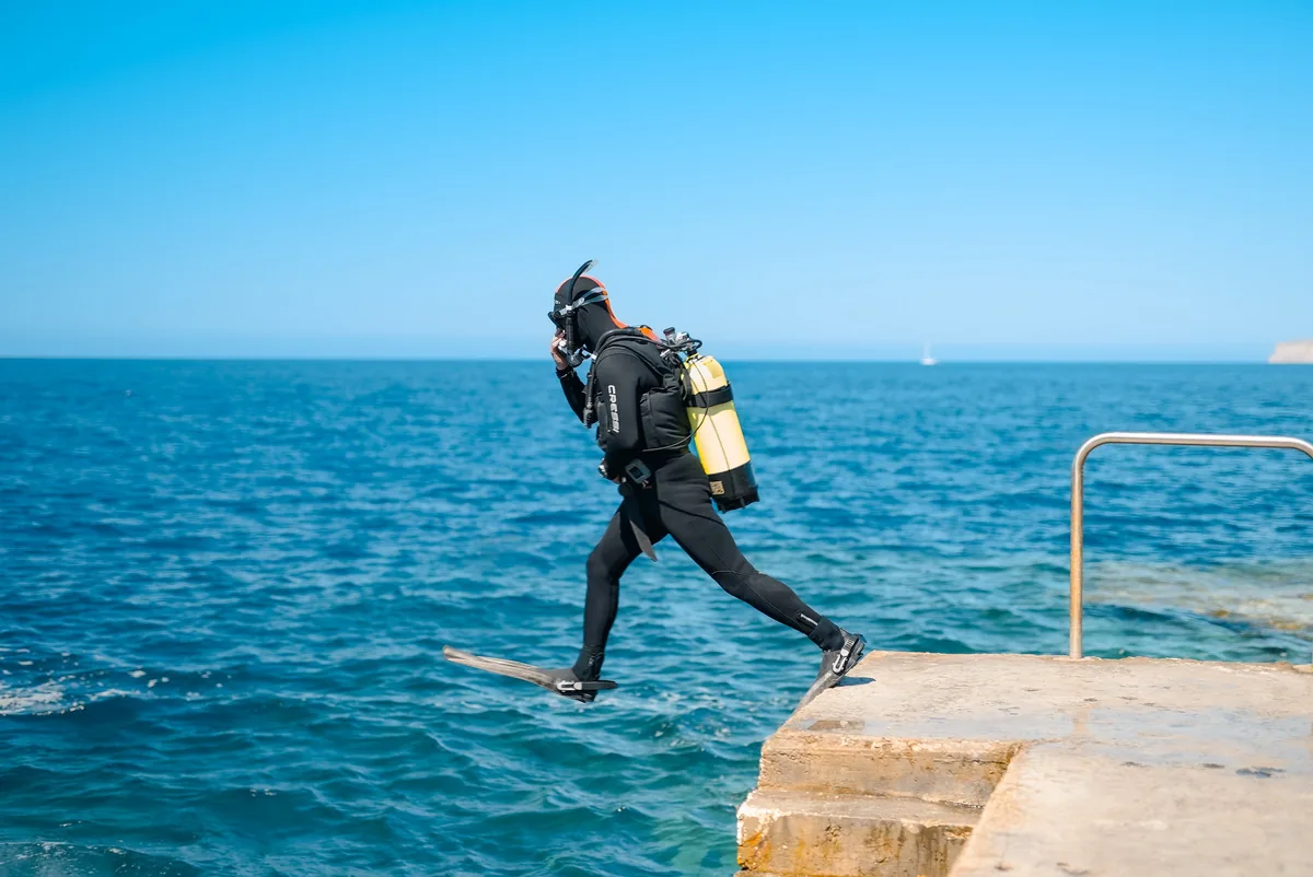 Buceador con equipo completo salta desde un muelle de piedra al mar azul