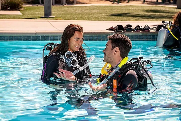 Instructora y alumno conversan dentro de la piscina con el equipo puesto