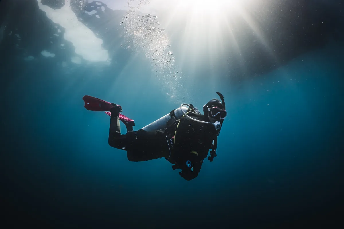 Buceador solitario desciende bajo rayos de sol en agua azul oscura