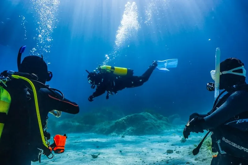Tres buceadores en agua azul clara, dos en primer plano y uno al fondo