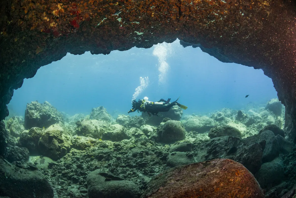 Buceador bajo un arco de roca cubierto de coral con luz entrando