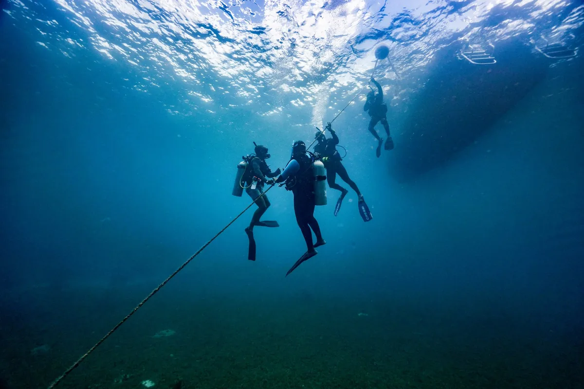 Grupo de buceadores en la línea de descenso bajo un barco, visto desde abajo