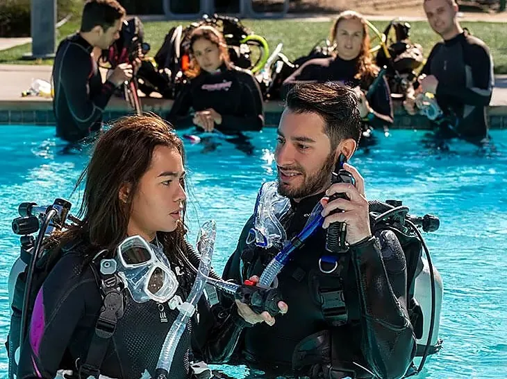 Instructora y alumno en la piscina con el grupo sentado en el borde