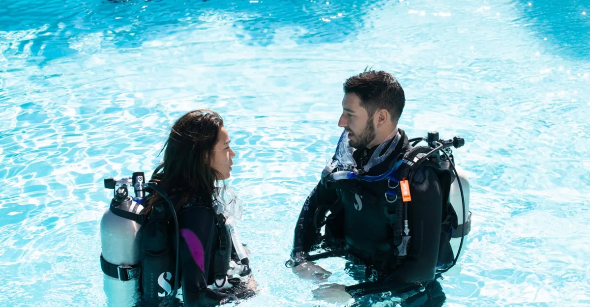 Dos buceadores hablan en una piscina de agua turquesa antes de una sesión