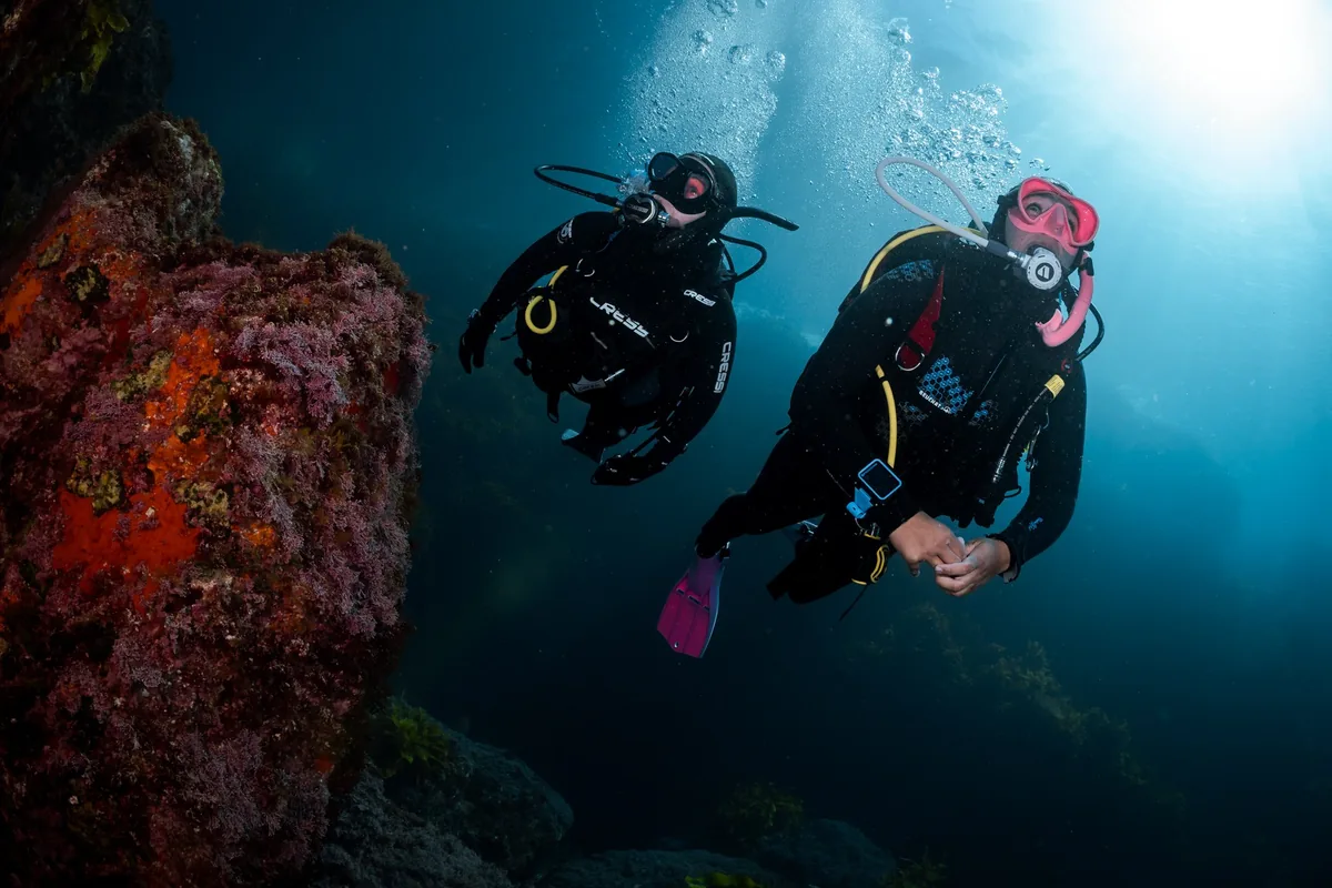 Dos buceadores nadan junto a una roca roja con la luz de la superficie