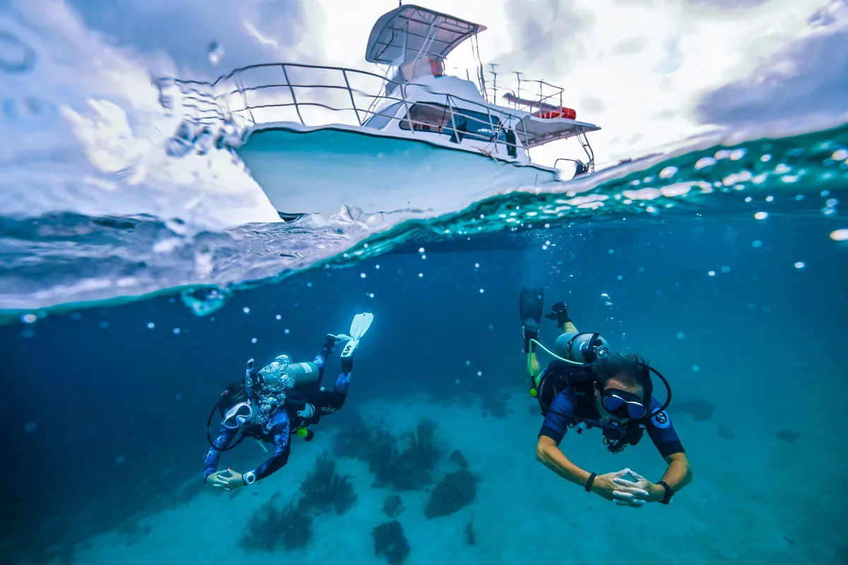 Barco visto desde el agua con dos buceadores nadando bajo la superficie sobre arena