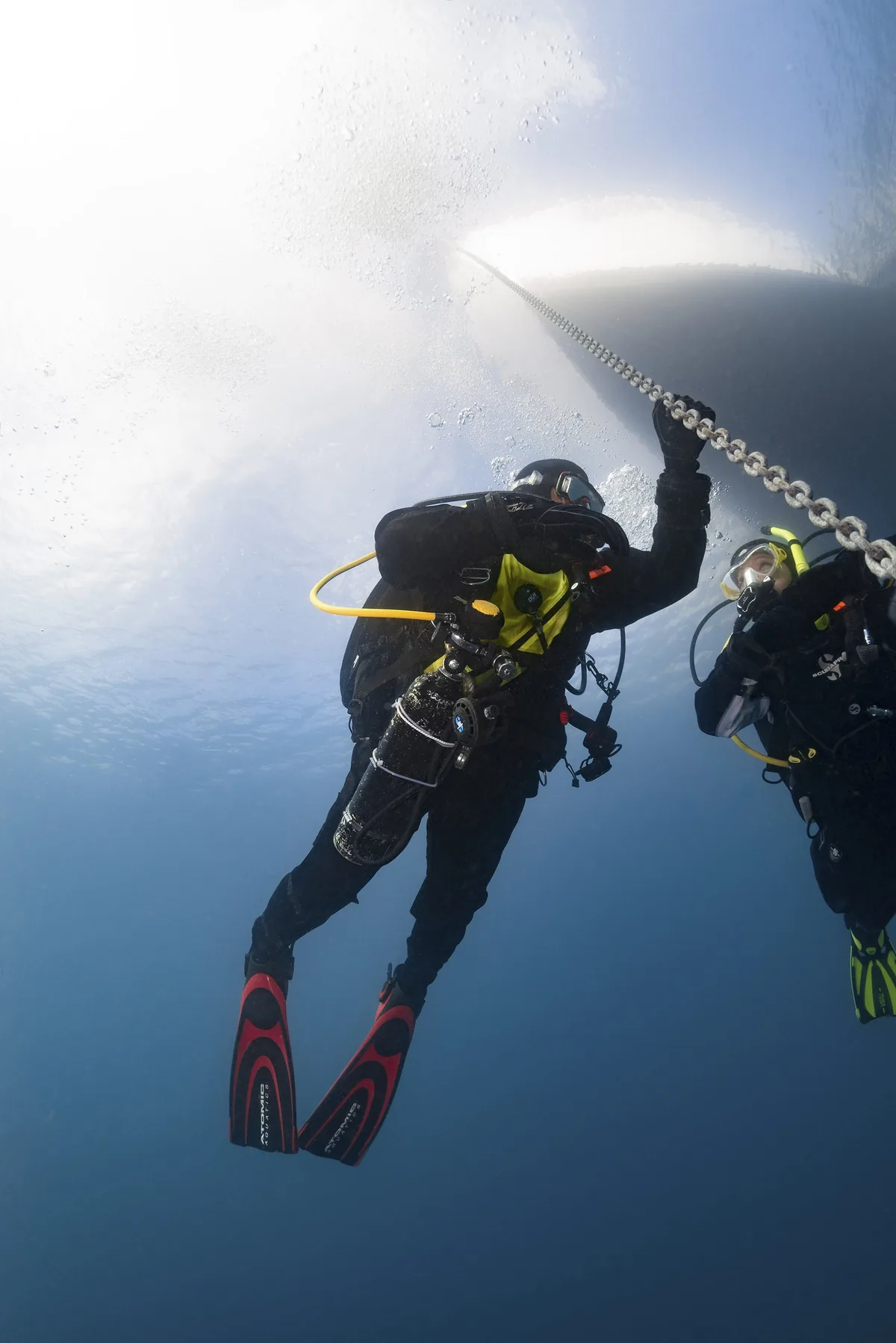 Dos buceadores descienden por un cabo bajo la luz de la superficie