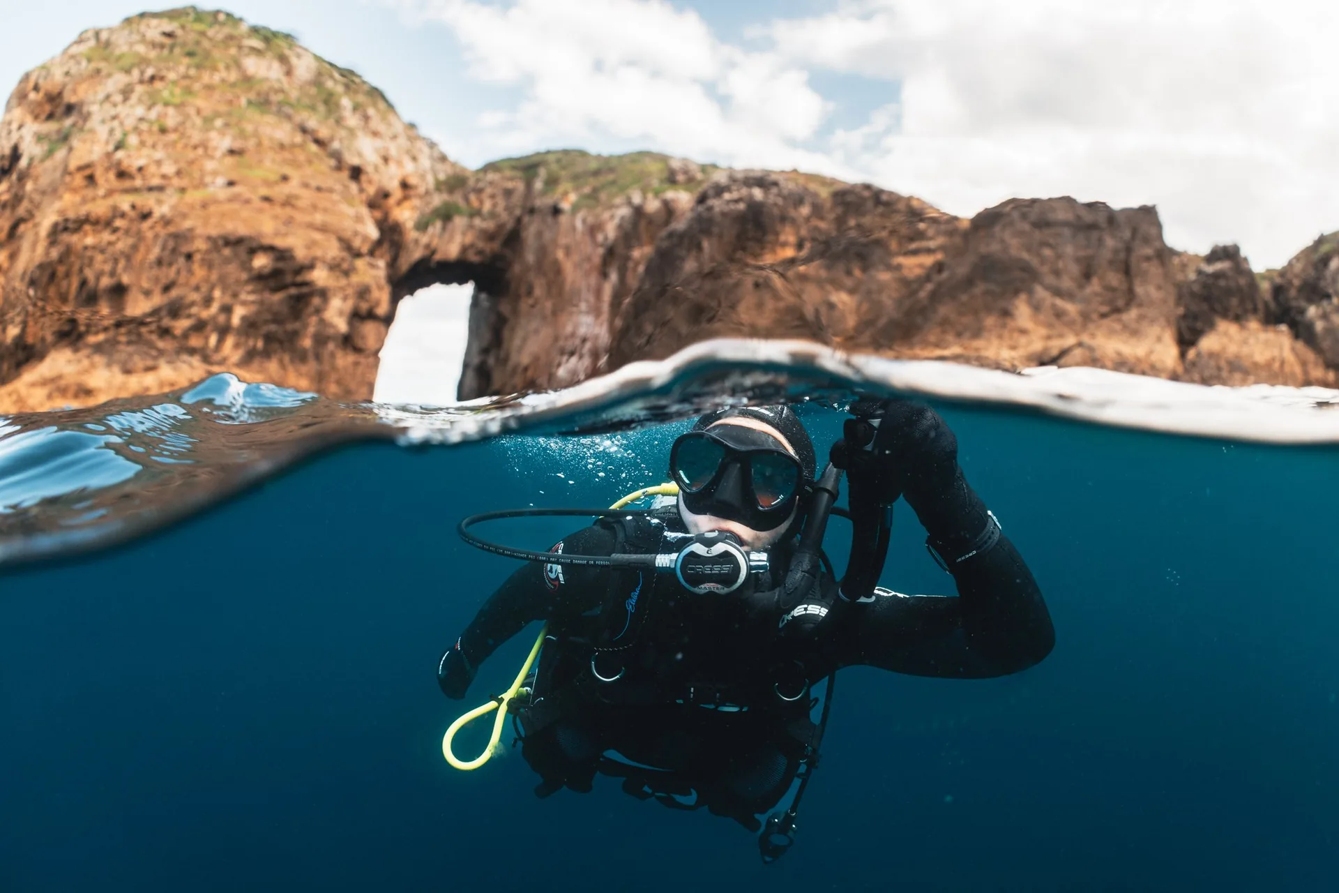 Buceador asoma a la superficie del mar con un arco natural de roca detrás