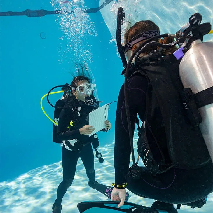Instructora con pizarra bajo el agua en la piscina y un buceador de espaldas