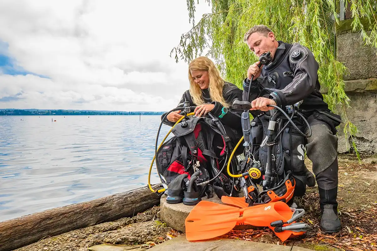 Instructora y alumno preparan sus equipos de traje seco junto a un lago